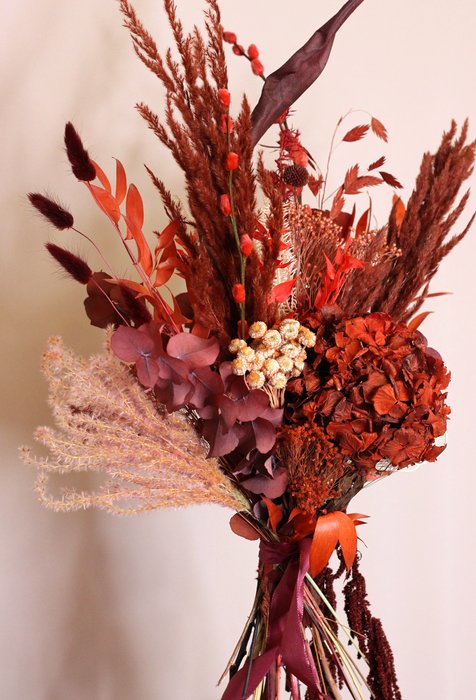 Dried Flower Bouquet in deep red tones and soft peach. Bouquet is standing against plain backdrop. Profile photo showing some of its flowers in details.