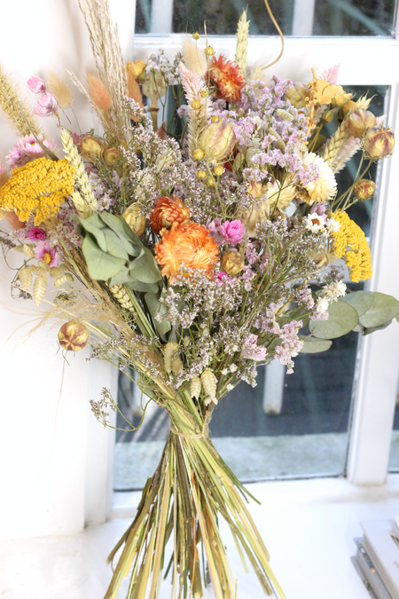 Picture shows a vibrant dried flower bouquet standing against window and white wall