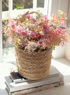 a woven jute basket filled with dried flowers (pink daisies and baby's breath) by window