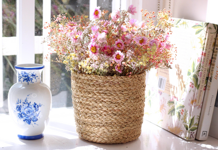 a woven jute basket filled with dried flowers (pink daisies and baby's breath) by window