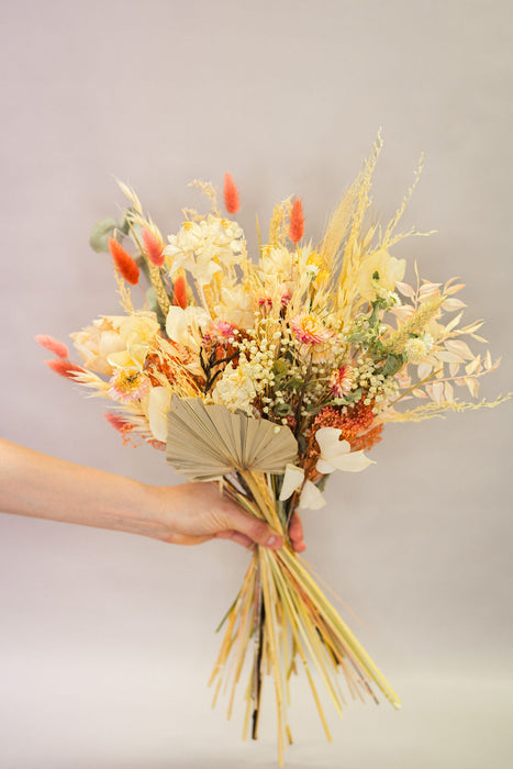 Hand holding a dried flower bouquet with natural and peach tones