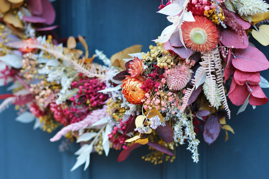 Close up of flowers in a mixed dried flower wreath against a blue door background