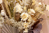 Close up of dried flower bouquet of mixed pale flowers against light peach background 