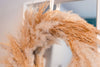 Close up of a dried flower pampas wreath in warm neutral tones hanging on a mirror in a white room