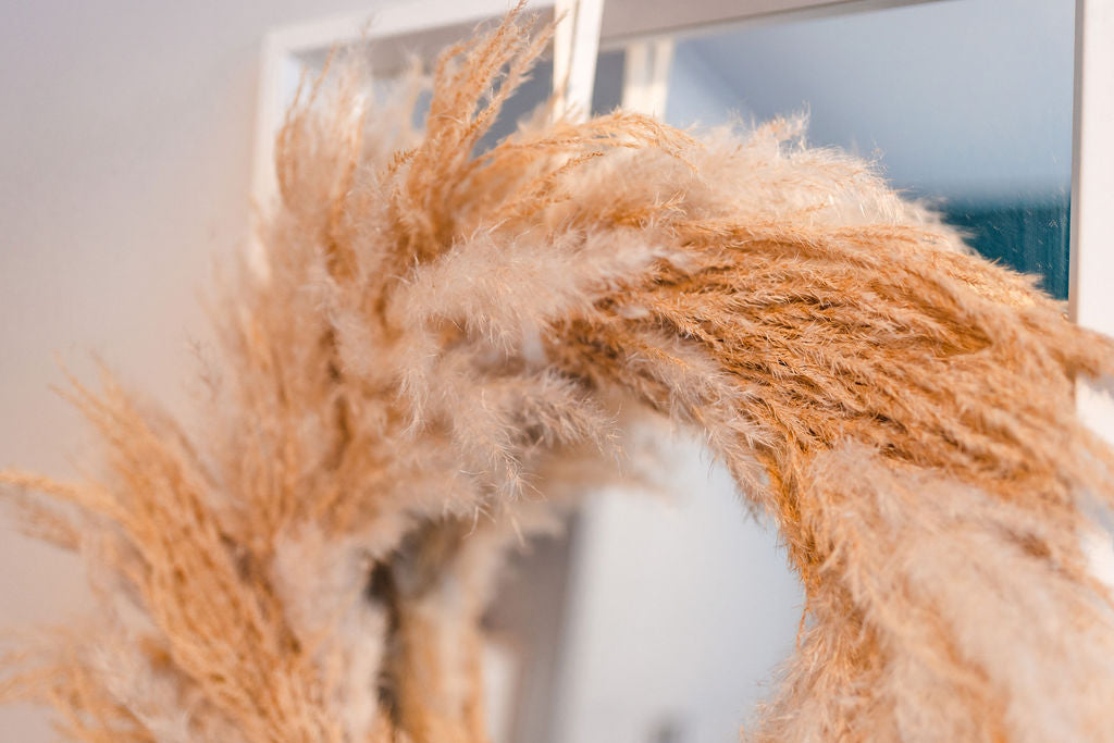 Close up of a dried flower pampas wreath in warm neutral tones hanging on a mirror in a white room