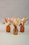 Set of three small coral ribbed glass jars filled with dried flowers and grasses in neutrals, peach and brown shades