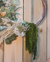 A dried flower wreath made up of eucalyptus, white ruscus, amaranthus and other dried flowers on a twisted wooden wreath.